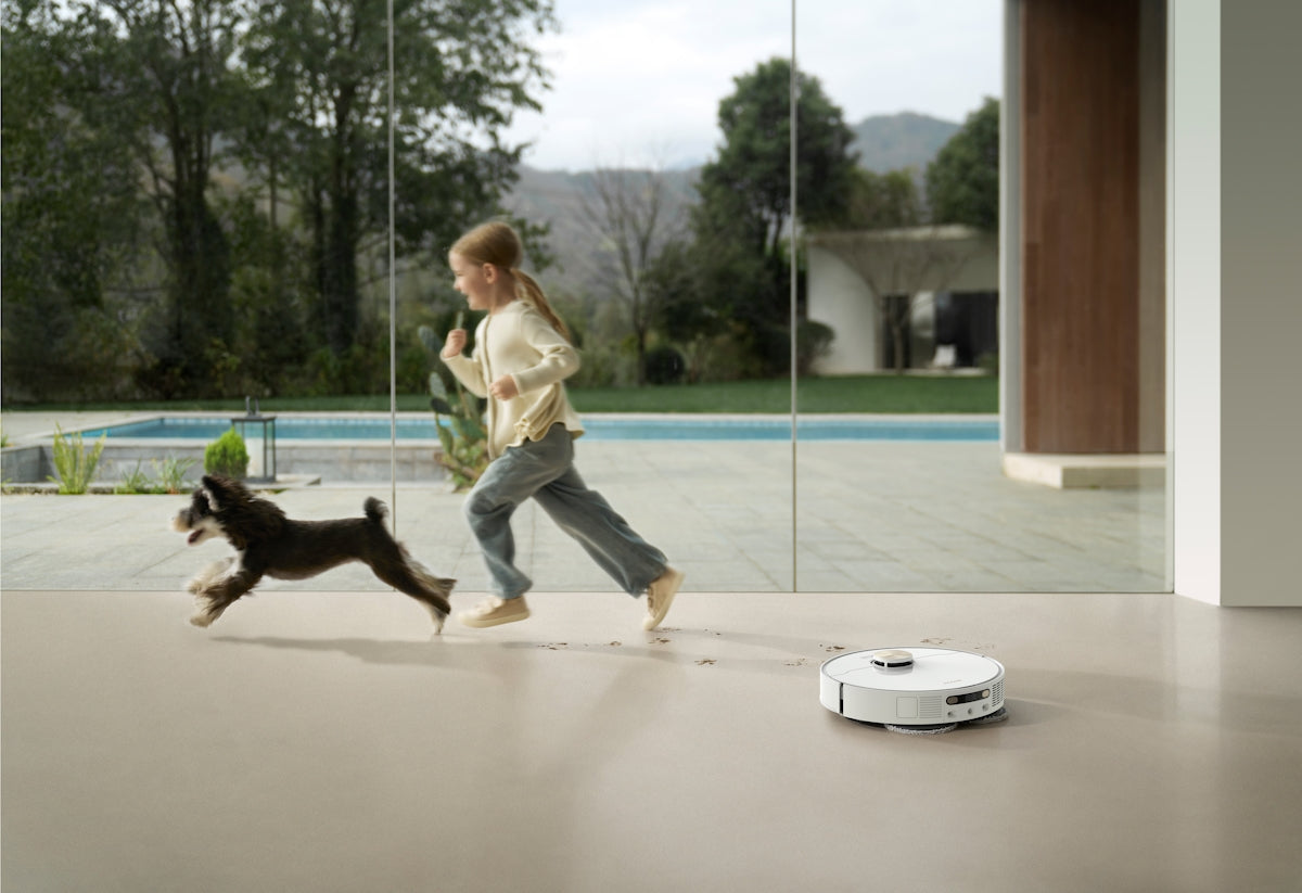Girl and dog run past robot vacuum cleaner