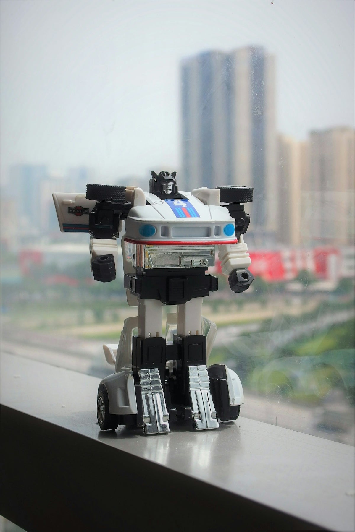 Toy robot on a ledge with a blurred city background.